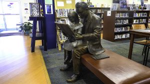 A bronze statue of a man reading to his daughter