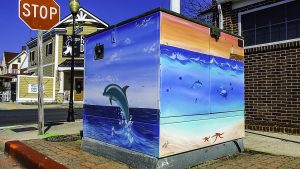 A Painted utility box with dolphins and a lighthouse